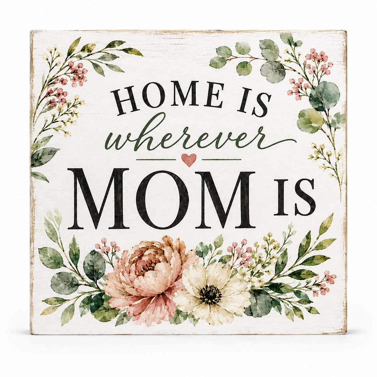 A square decorative sign with a distressed white background featuring the phrase 'HOME IS wherever MOM IS' in black and green lettering with a small pink heart, surrounded by watercolor-style floral and leafy illustrations.