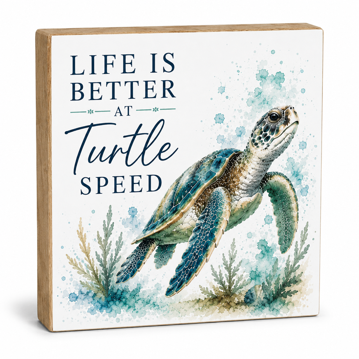 Square decorative sign with a light wood border and a white face featuring the phrase “LIFE IS BETTER AT Turtle SPEED” in navy lettering beside a painted sea turtle in blue-green tones with small seagrass illustrations.