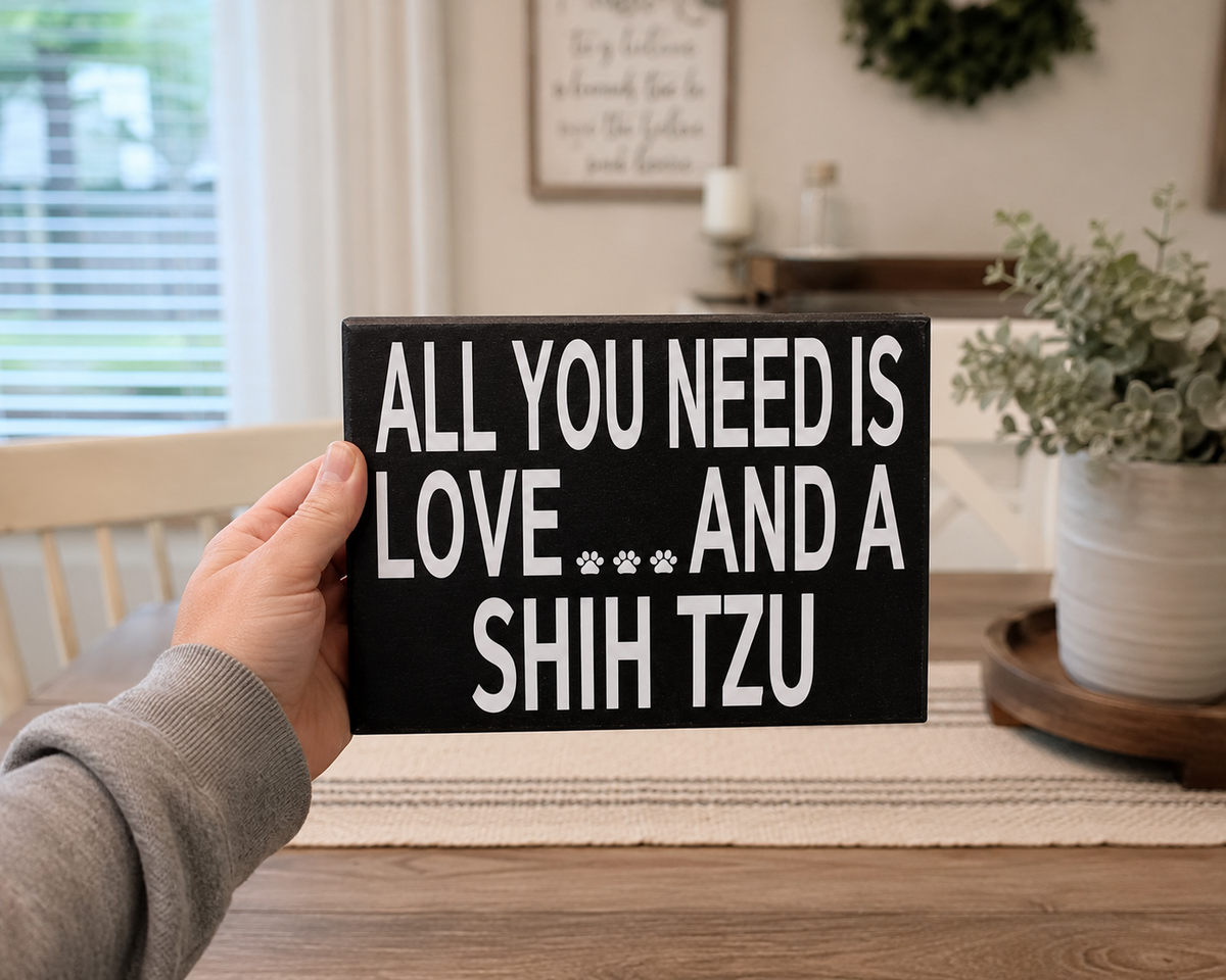 A hand holding a black rectangular sign with white text that reads 'ALL YOU NEED IS LOVE.