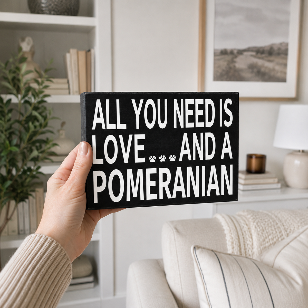 A hand holds a black rectangular sign with bold white text reading 'ALL YOU NEED IS LOVE.