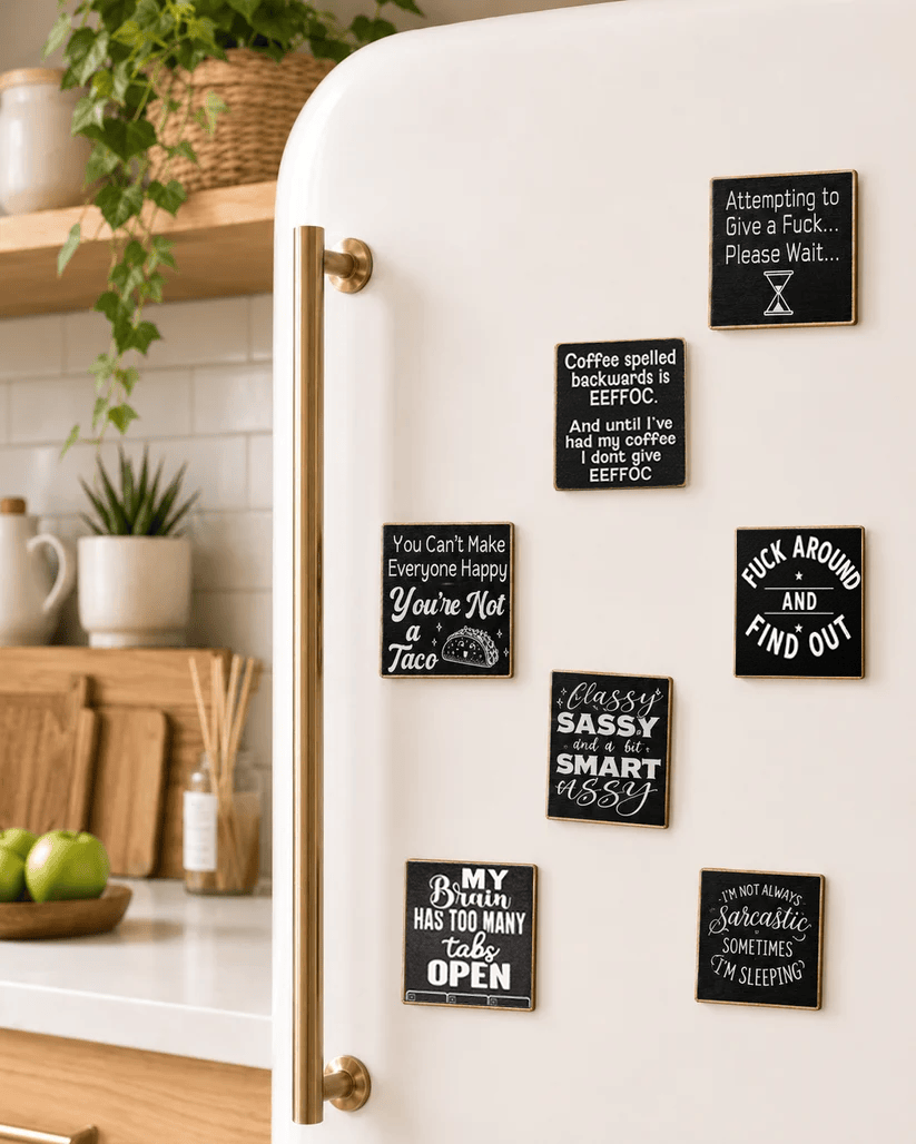 A set of black square refrigerator magnets with humorous and sarcastic phrases in white script and block lettering, shown on a white retro-style refrigerator in a bright kitchen setting.