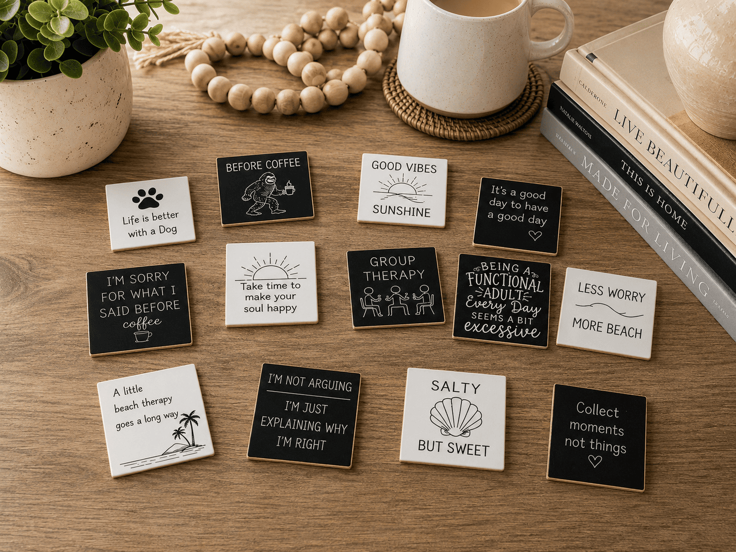 A styled flat-lay of multiple small square printed cards or stickers with humorous quotes and simple line drawings, arranged on a wooden tabletop with a mug, books, beads, and a plant in the background.
