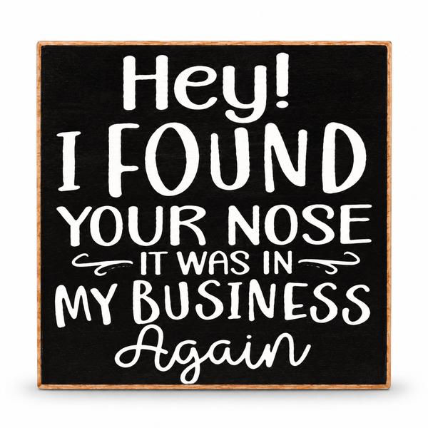 A square black decorative sign with a light wood border and white hand-lettered text that reads, 'Hey! I FOUND YOUR NOSE IT WAS IN MY BUSINESS Again.'.