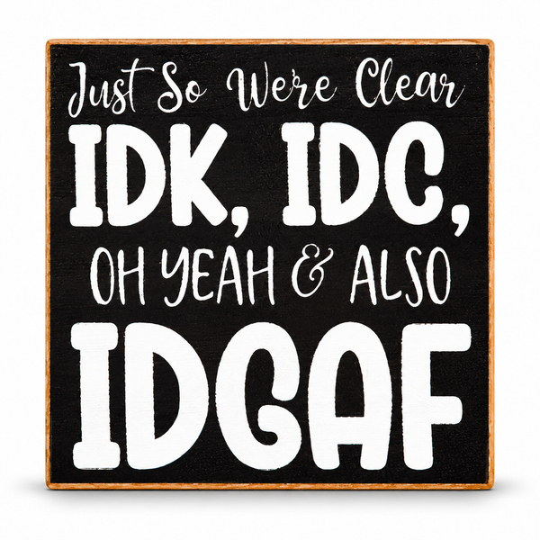 Square decorative sign with a black face, white hand-lettered text reading 'Just So Were Clear IDK, IDC, OH YEAH & ALSO IDGAF', and a light natural wood border on a white background.