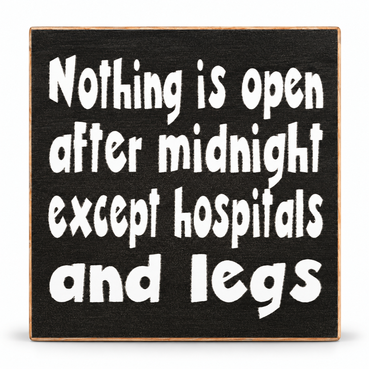 A square black wooden sign with a natural wood border and white hand-painted text that reads, 'Nothing is open after midnight except hospitals and legs.'.