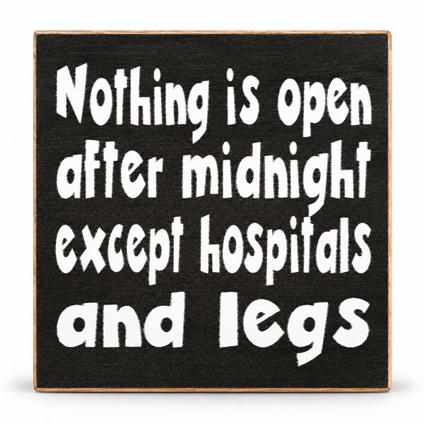 A square black wooden sign with a natural wood border and white hand-painted text that reads, 'Nothing is open after midnight except hospitals and legs.'.