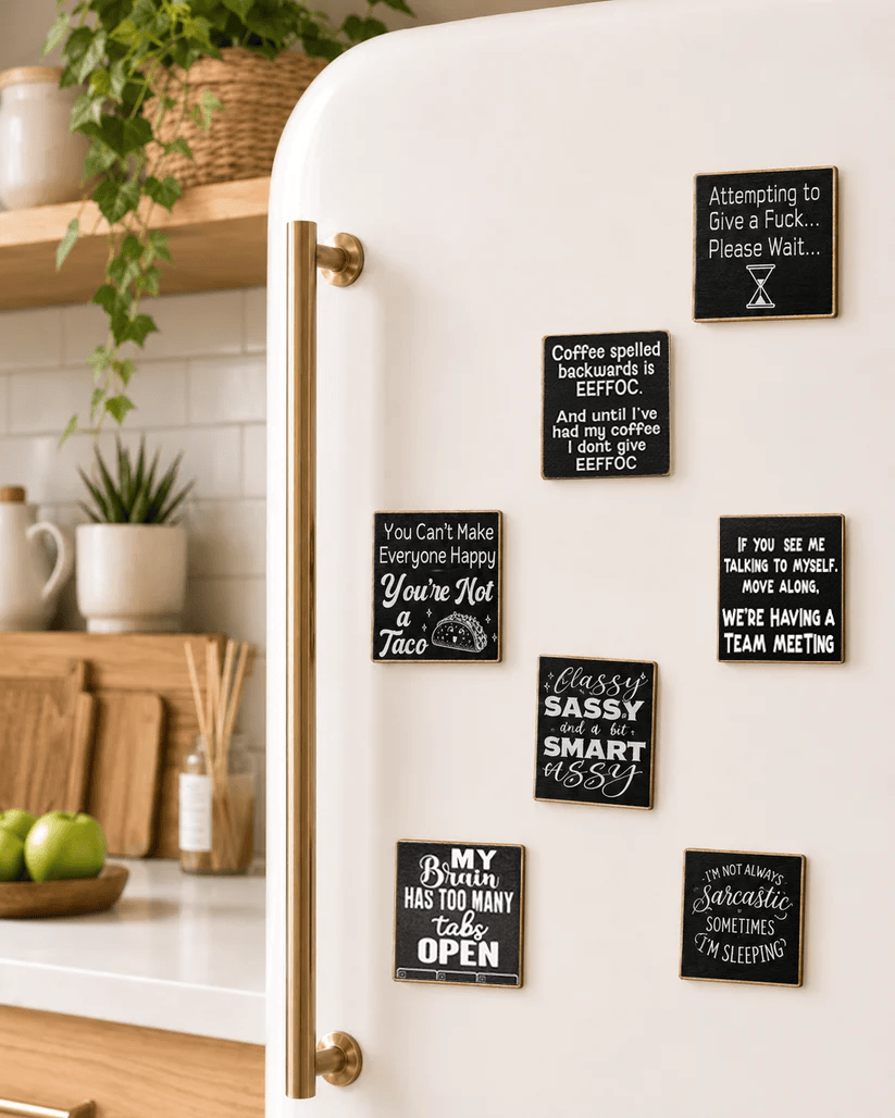 A white refrigerator in a bright kitchen setting, decorated with multiple black square magnets featuring humorous and witty sayings in white script and block lettering.