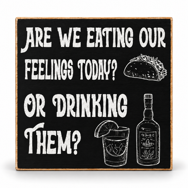 A square decorative sign with a black chalkboard-style background and a light wood border. White distressed text reads, "ARE WE EATING OUR FEELINGS TODAY? OR DRINKING THEM?" with line drawings of a taco, a drink with a lime slice, and a liquor bottle.