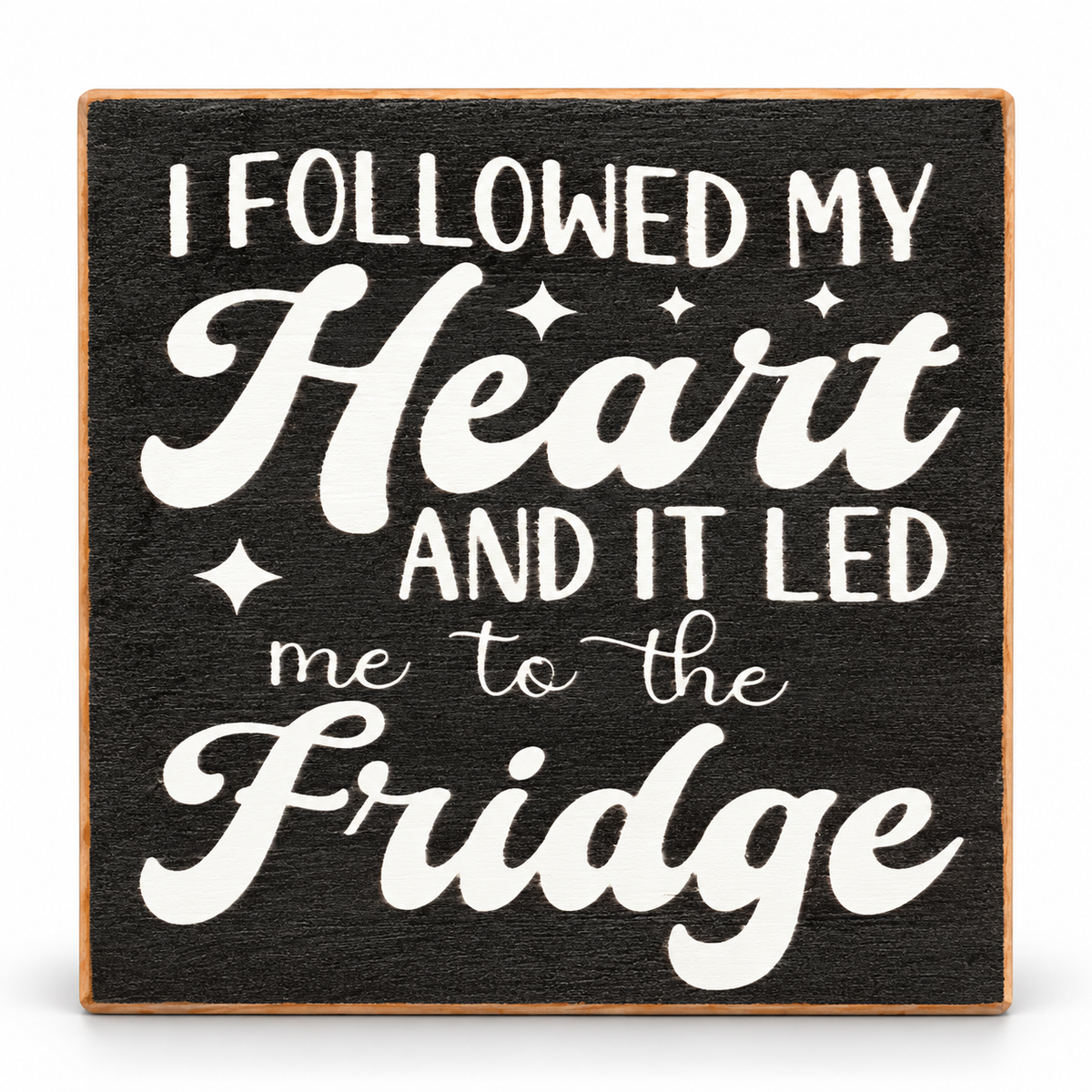 A square decorative sign with a dark charcoal-textured background and a light wood border. White lettering reads, 'I FOLLOWED MY Heart AND IT LED me to the Fridge' with small star accents.
