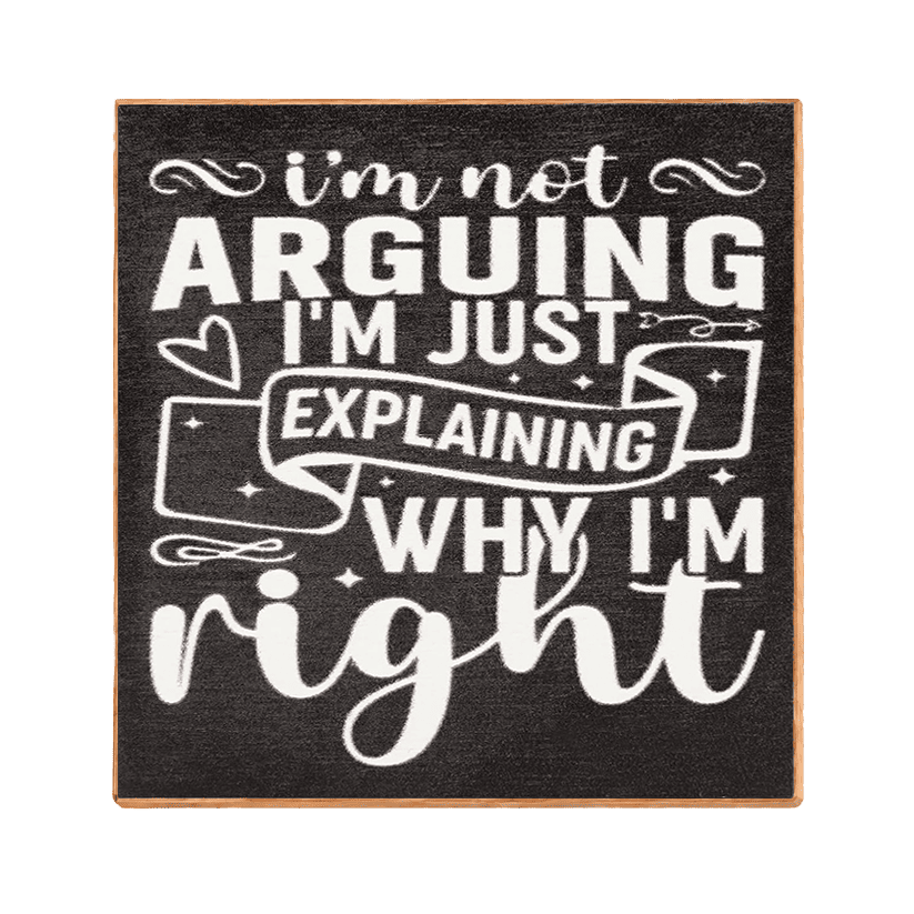 Square decorative wall sign with a dark charcoal background and white typographic text reading, "i'm not ARGUING I'M JUST EXPLAINING WHY I'M right," with small decorative heart, ribbon, and star motifs. The sign has a thin natural wood edge and is shown centered on a plain white background.