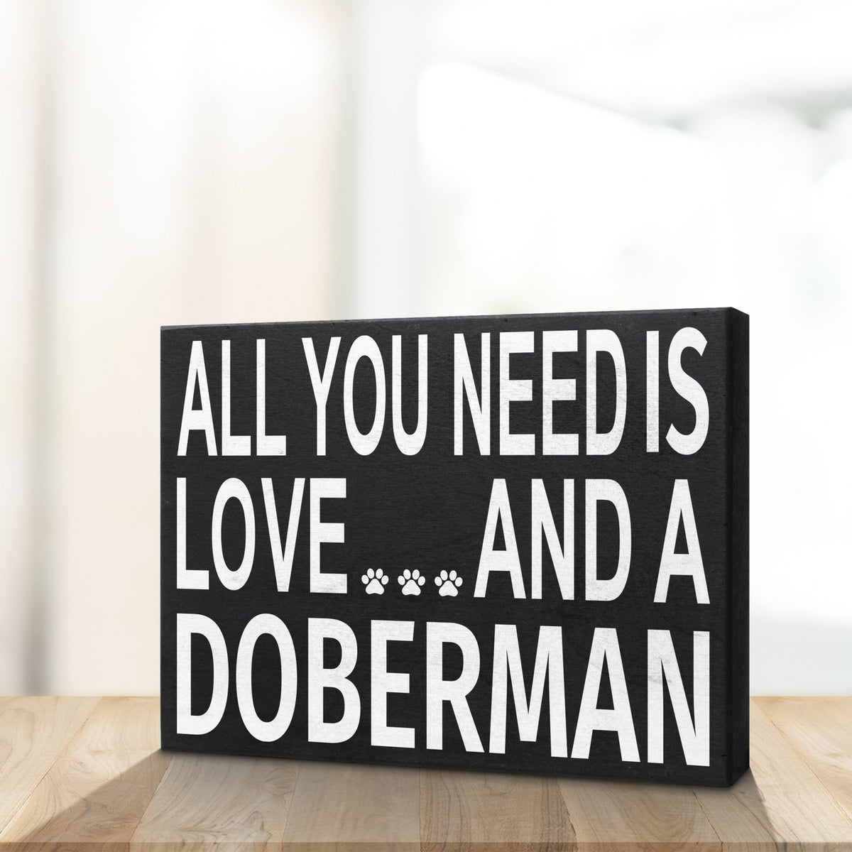 Decorative sign with text 'All you need is love and a Doberman' on a wooden surface.