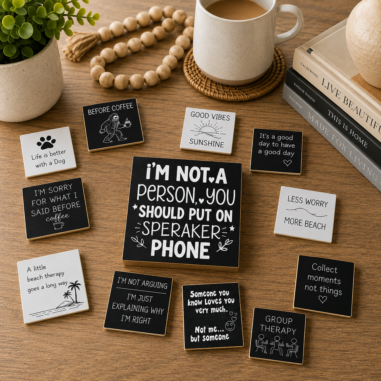 A styled flat-lay of multiple small square white and black enamel pins with humorous quotes and illustrations, arranged on a wooden tabletop next to a mug, beads, a plant, and books.