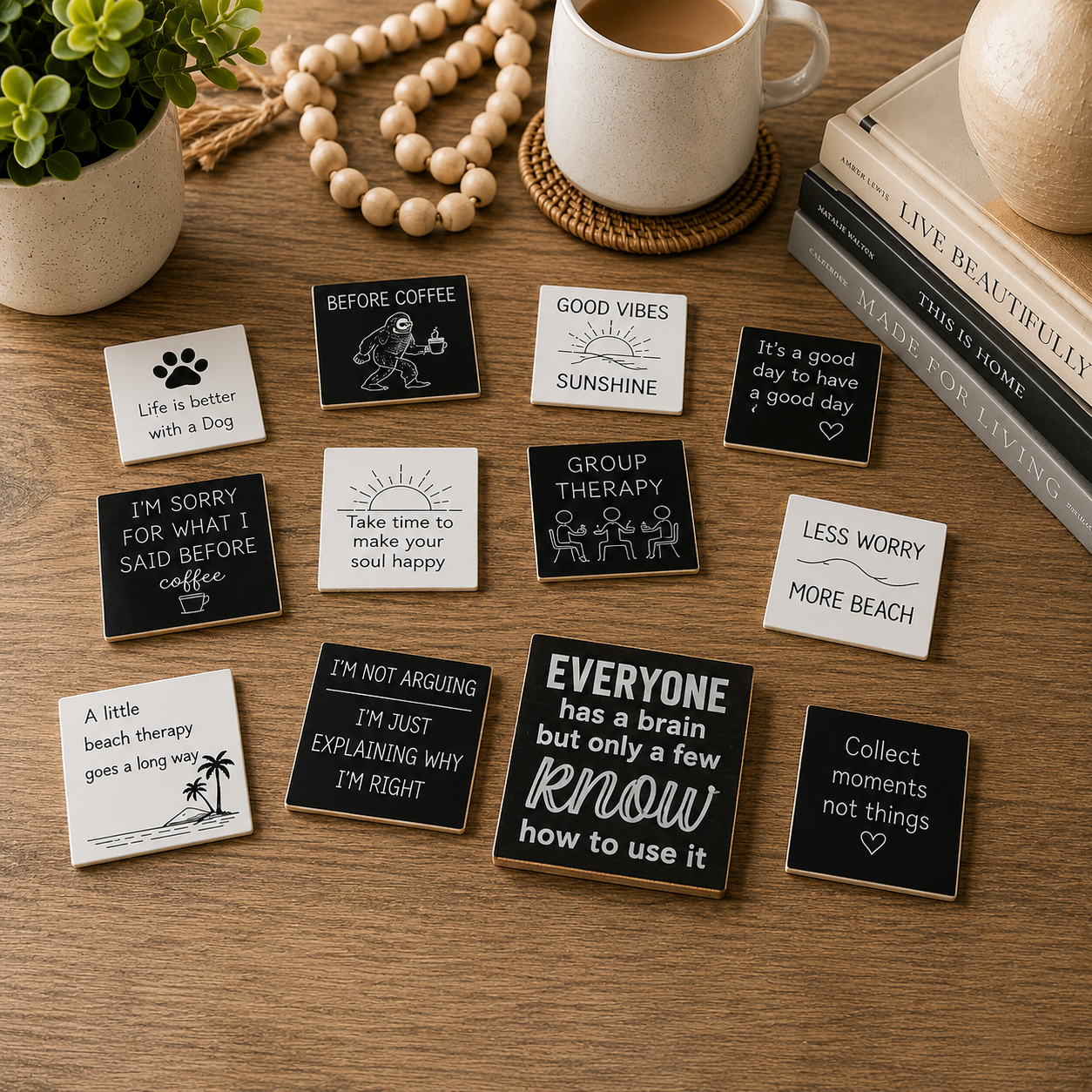 A styled flat-lay of multiple small square ceramic coasters with humorous quotes and simple line drawings, arranged on a wooden tabletop with a mug, books, beads, and a plant nearby.