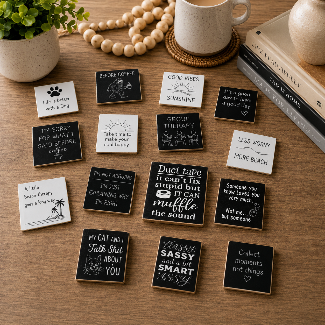 A set of small square black and white printed cards or tags with humorous quotes and simple illustrations, arranged on a wooden tabletop with a mug, books, beads, and a plant nearby.