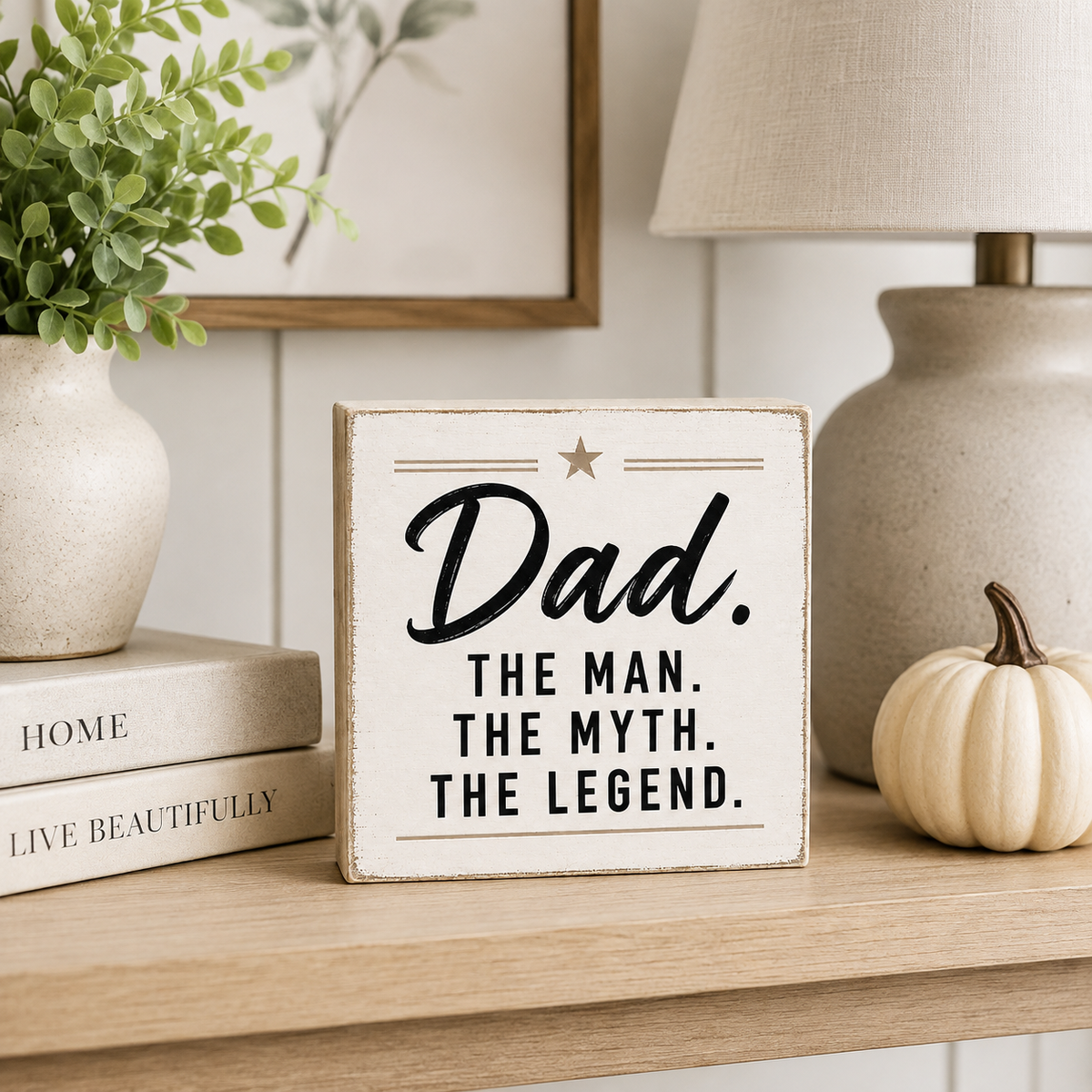 A square white wooden sign with a distressed finish and black text reading “Dad. THE MAN.