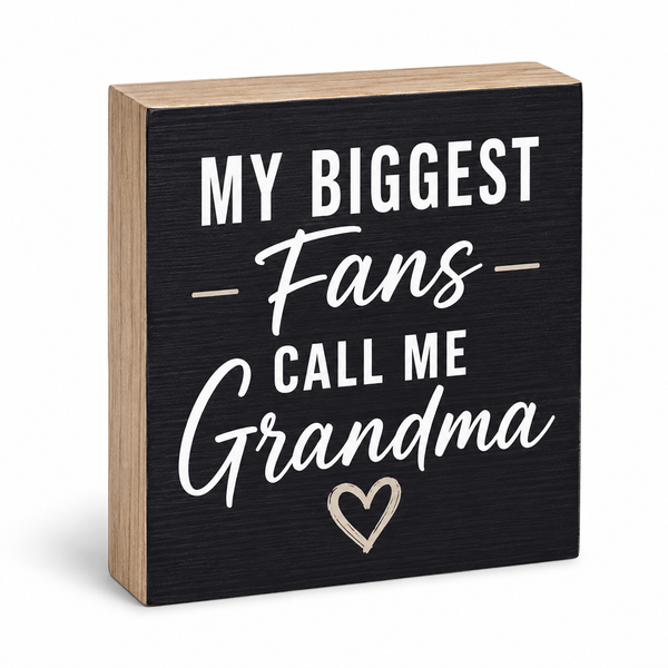 A square decorative wooden sign with a black front panel and natural wood sides, printed with the phrase “MY BIGGEST Fans CALL ME Grandma” in white lettering, plus a small outlined heart near the bottom, shown on a white background.