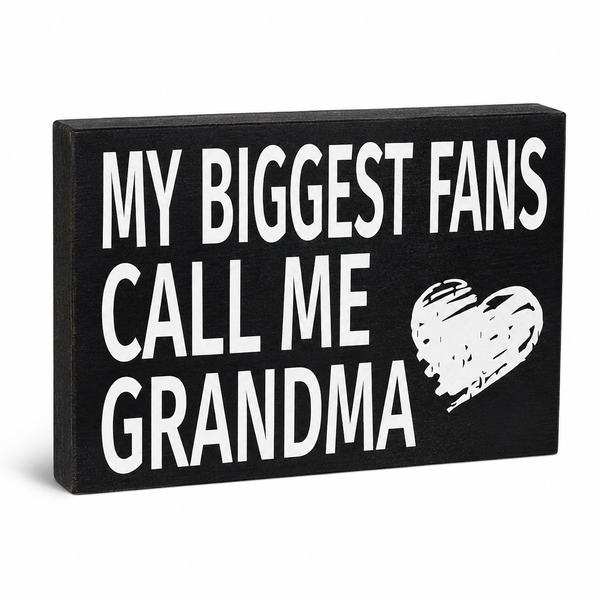 A rectangular black wooden sign with bold white text reading 'MY BIGGEST FANS CALL ME GRANDMA' and a white heart graphic, shown on a clean white background.