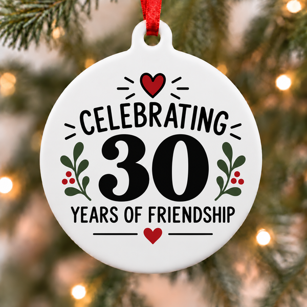 White round Christmas ornament reading Celebrating 30 Years of Friendship with red hearts and green leaves hanging on a decorated tree