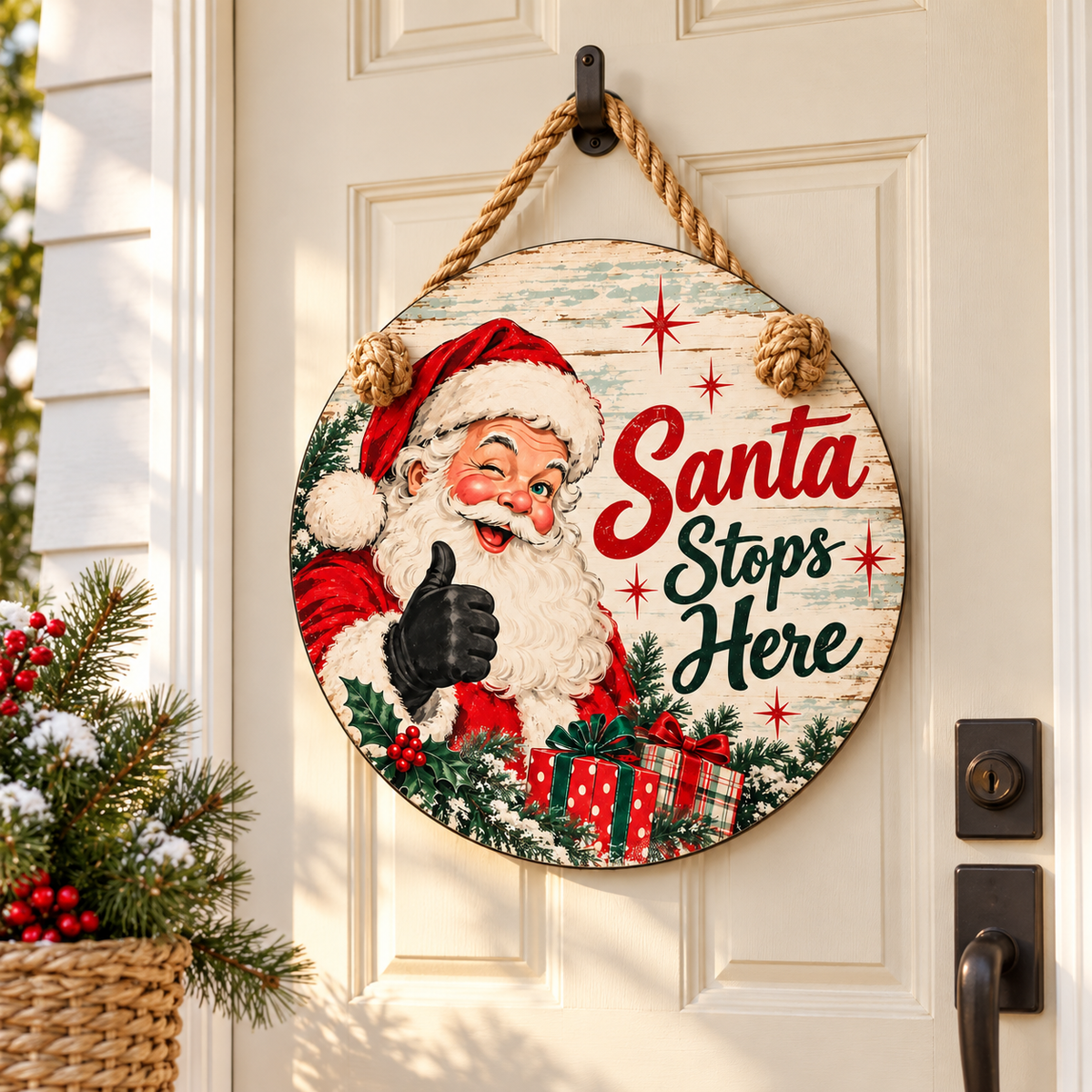 Santa Stops Here round Christmas door hanger on a cream door with festive greenery