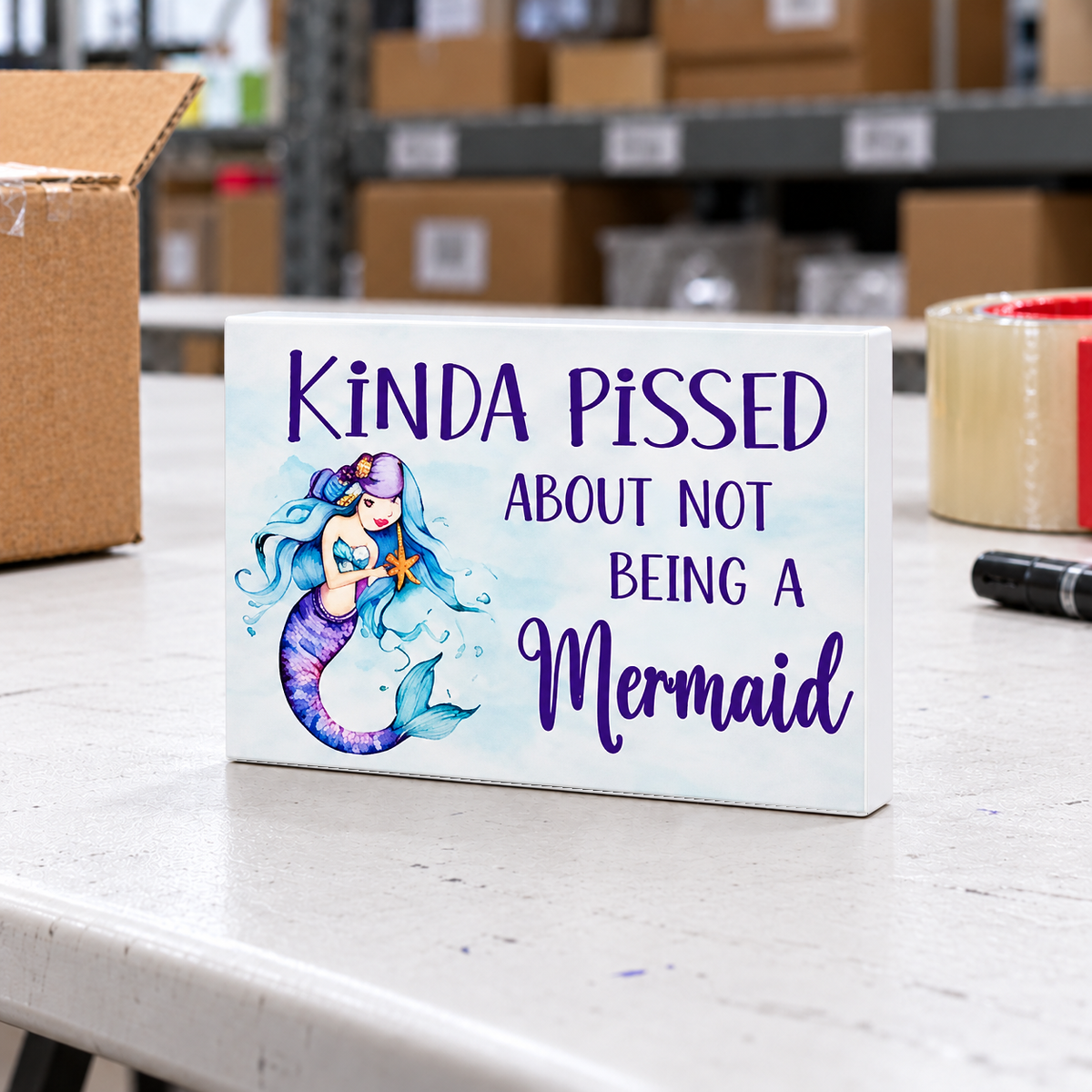Kinda Pissed About Not Being a Mermaid magnet and mini sign on a white folding warehouse table.
