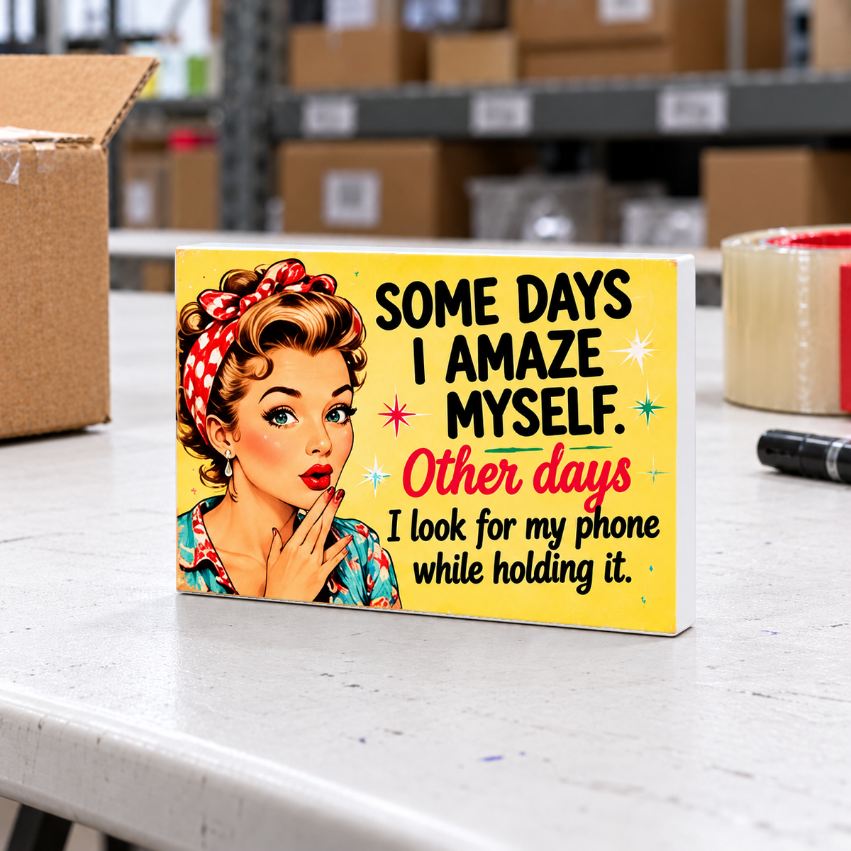 Some Days I Amaze Myself. Other Days I Look for My Phone While Holding It magnet and mini sign on a white folding warehouse table.