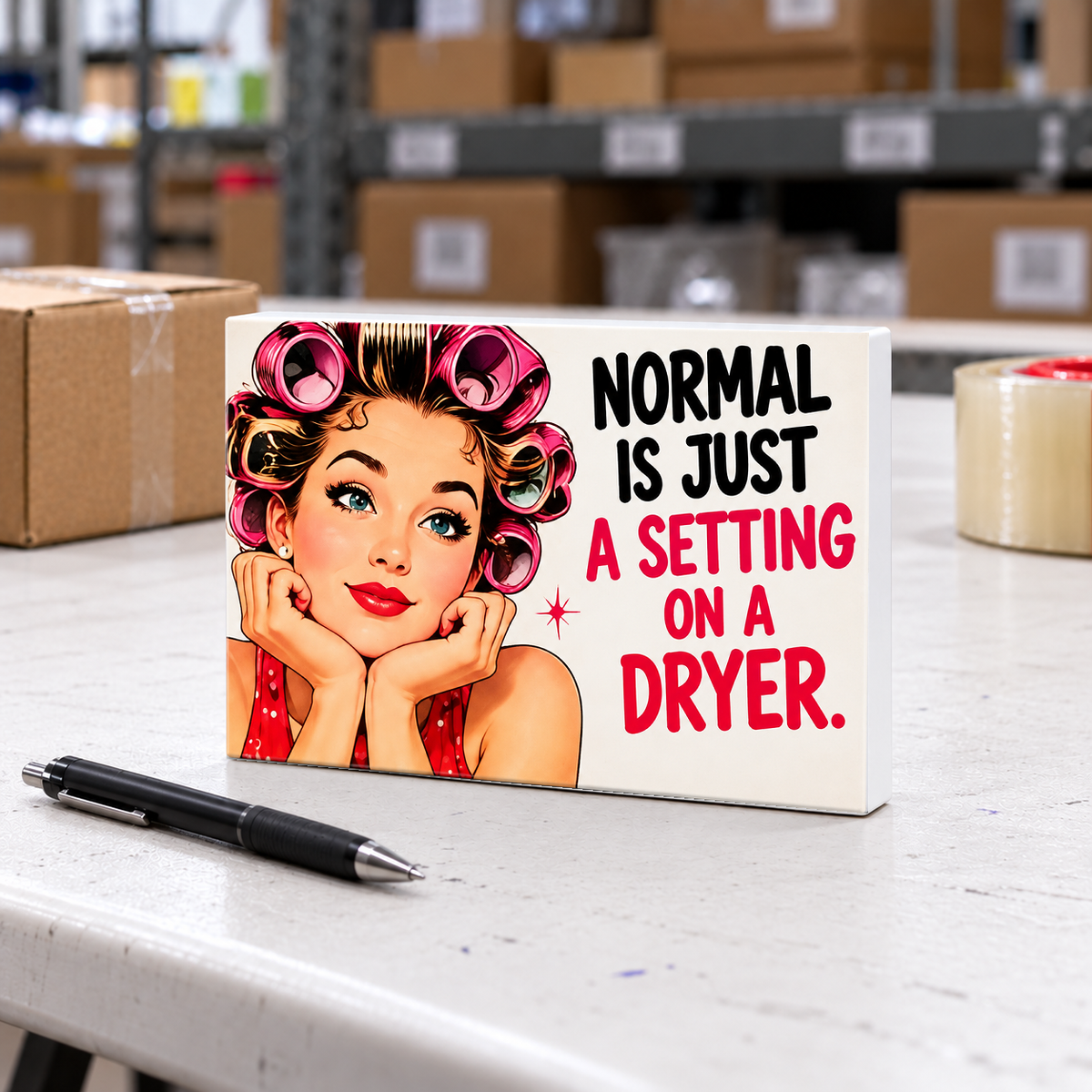 Normal Is Just a Setting on a Dryer magnet and mini sign on a white folding warehouse table.