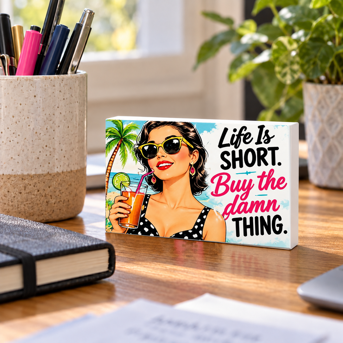 Life Is Short. Buy the Damn Thing mini sign standing on a desk with white PVC edges.