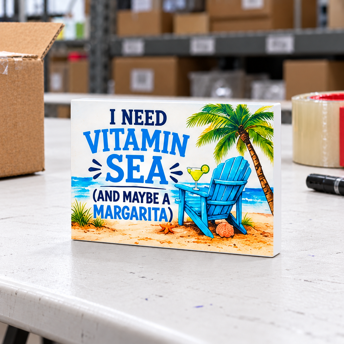 I Need Vitamin Sea (And Maybe a Margarita) mini sign on a white folding warehouse table with packing supplies.