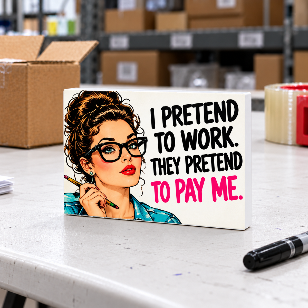 I Pretend to Work They Pretend to Pay Me mini sign on a white folding warehouse table with packing supplies.