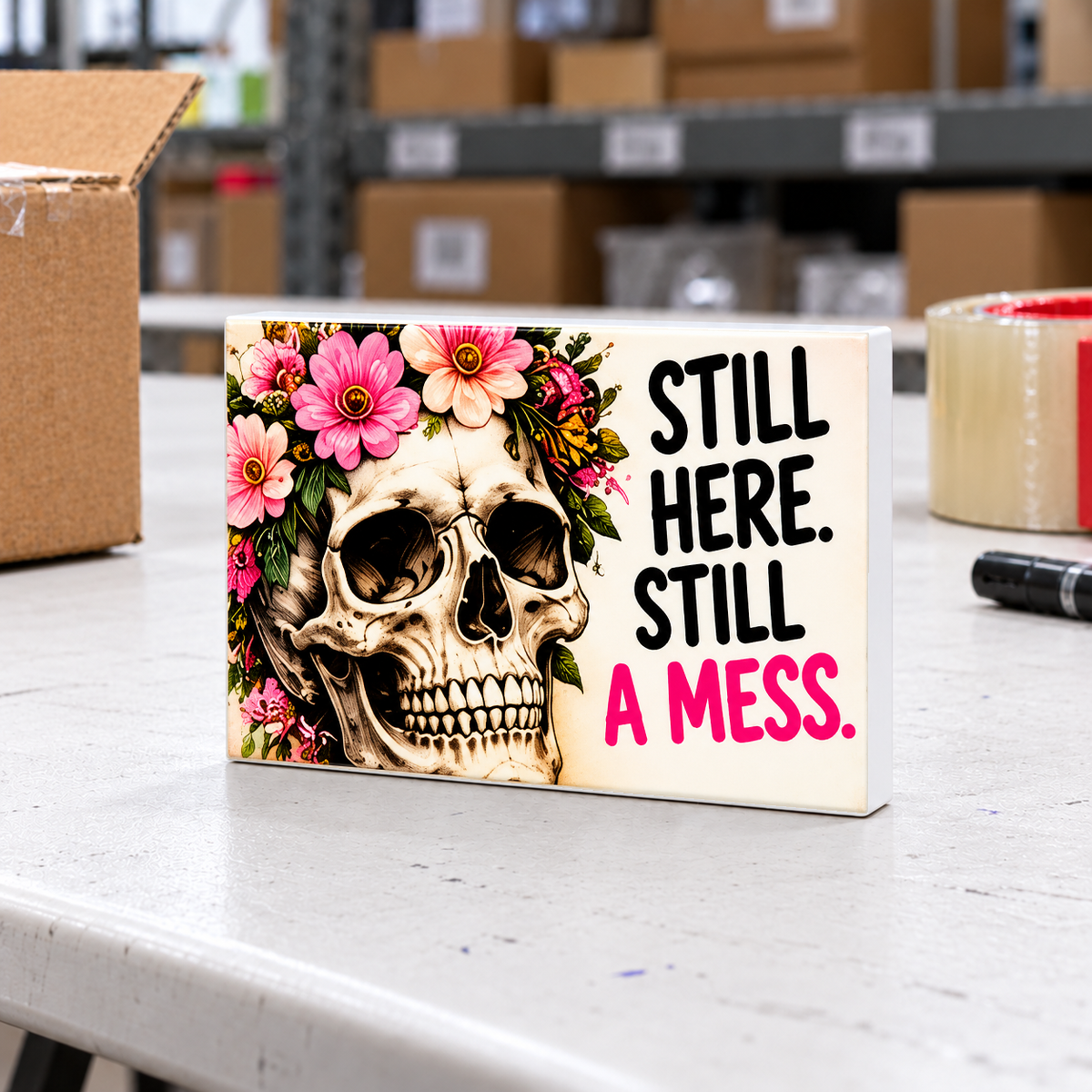 Still Here Still a Mess magnet and mini sign on a white folding warehouse table.