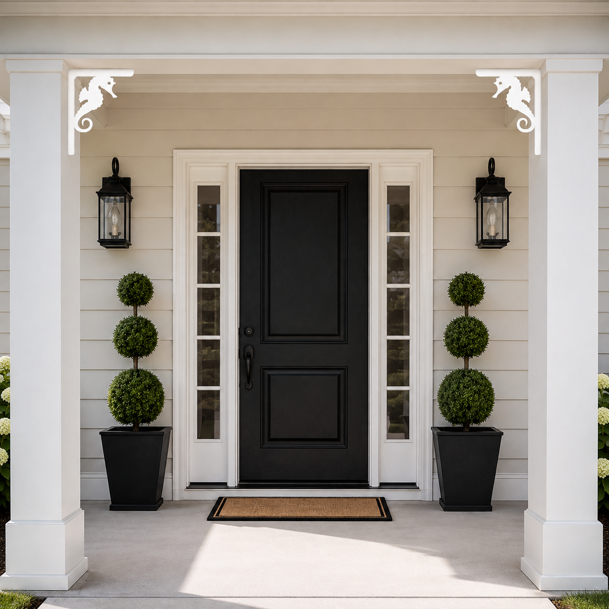 Front porch entryway with a black paneled door centered between white sidelight panels, flanked by two black lantern wall sconces and matching black planters with topiary trees. The house siding is light beige, and a tan doormat sits in front of the door.