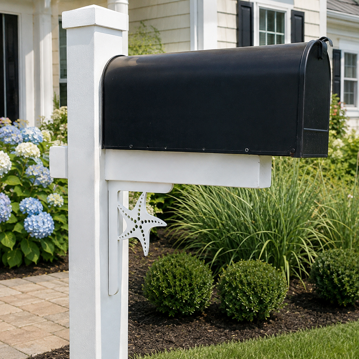 A black mailbox mounted on a white custom post in a landscaped garden bed in front of a house.