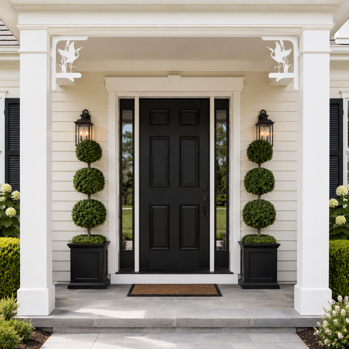 A front porch entryway with a black paneled door centered between white columns, flanked by black planter boxes with tall green topiary trees and black wall lanterns.