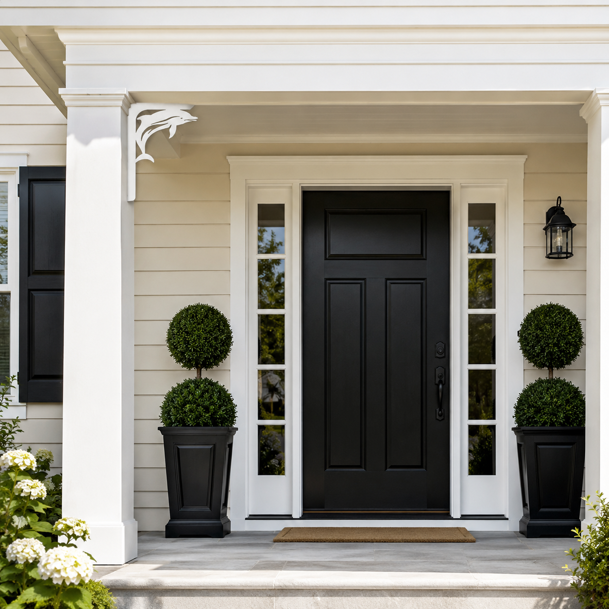 A black front door with white trim, flanked by tall black planters with rounded green topiary trees, set on a porch with beige house siding and a white column.