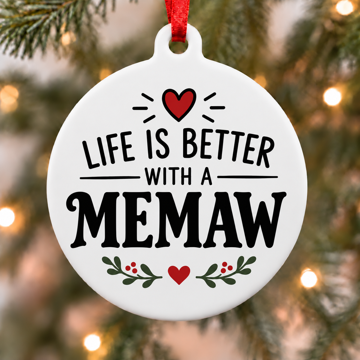 White round Christmas ornament reading Life Is Better With a Memaw, with red hearts and green botanical accents hanging on a Christmas tree